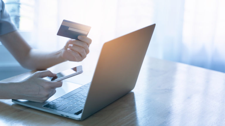 Young woman holding credit card and using laptop computer. Businesswoman working at home